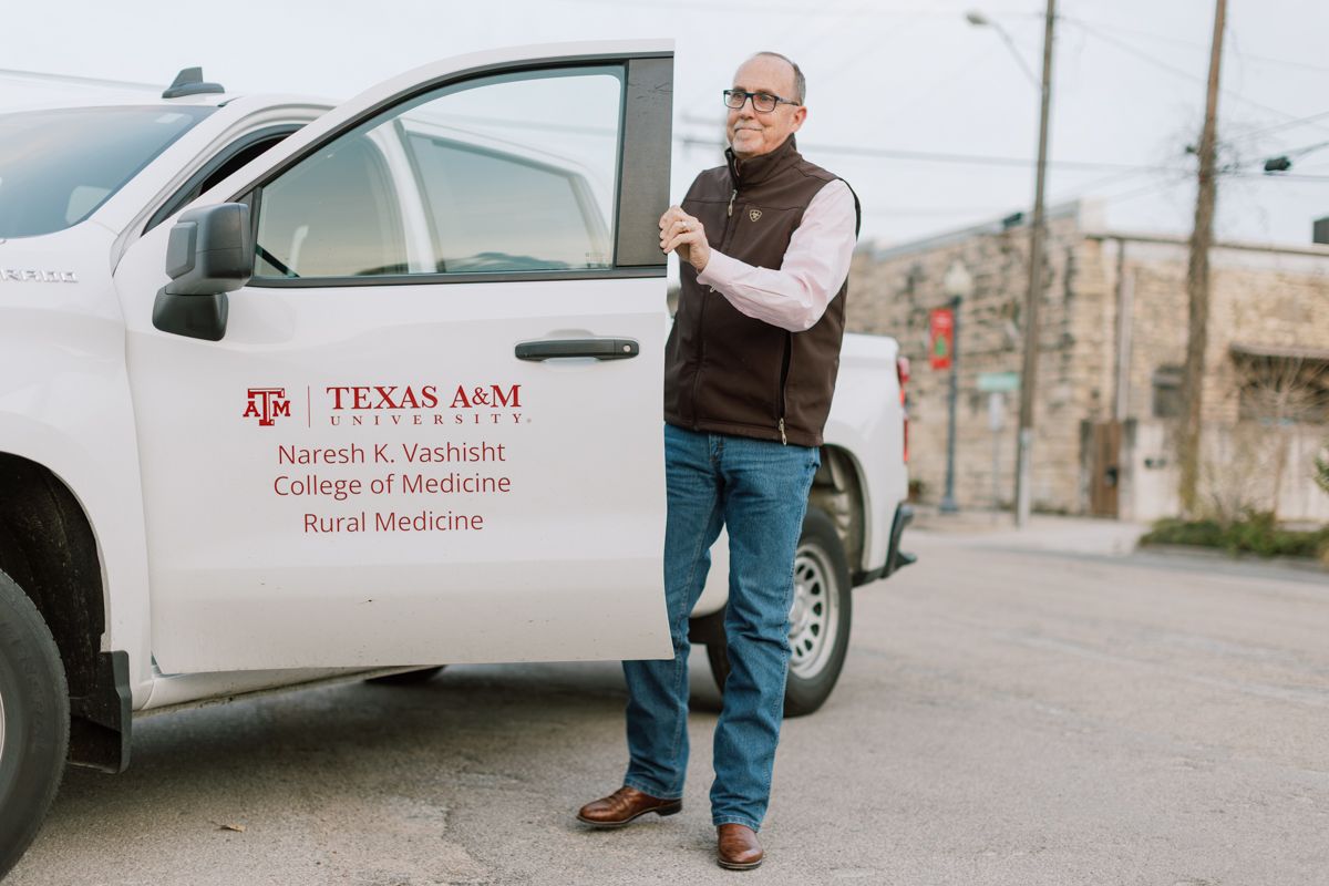 A man stands beside a Texas A&M College of Medicine Rural Medicine branded pickup truck outdoors.