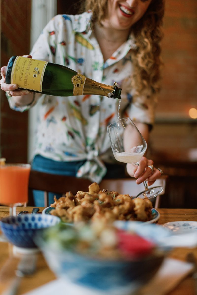 Woman pouring champagne into a wine glass at a festive dining table with appetizers and drinks.