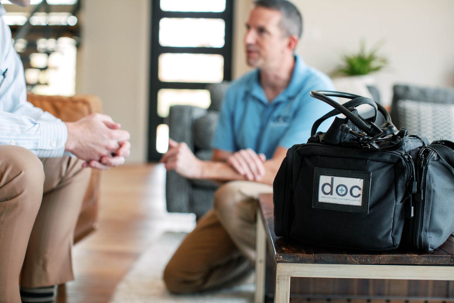 Two men having a conversation in a living room with a black doc medical bag in the foreground.