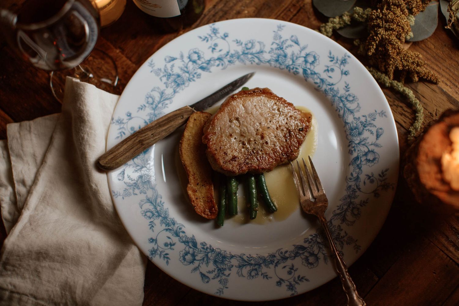 Elegant plated dish with seared meat, asparagus, and sauce on blue floral china with vintage silverware.