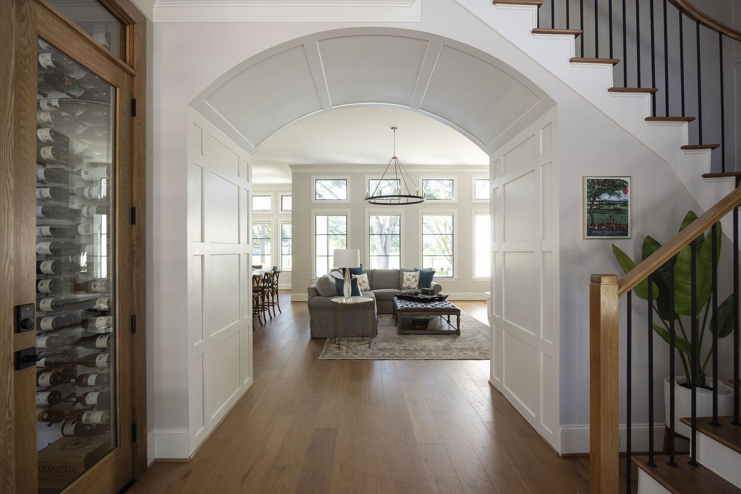 Elegant home entryway with arched doorway, hardwood floors, wainscoting, chandelier, and staircase leading to bright living room.