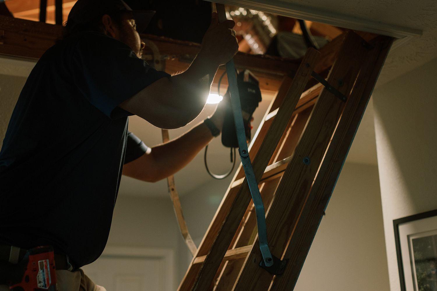 Technician using power tool on wooden attic ladder installation in home ceiling access point.