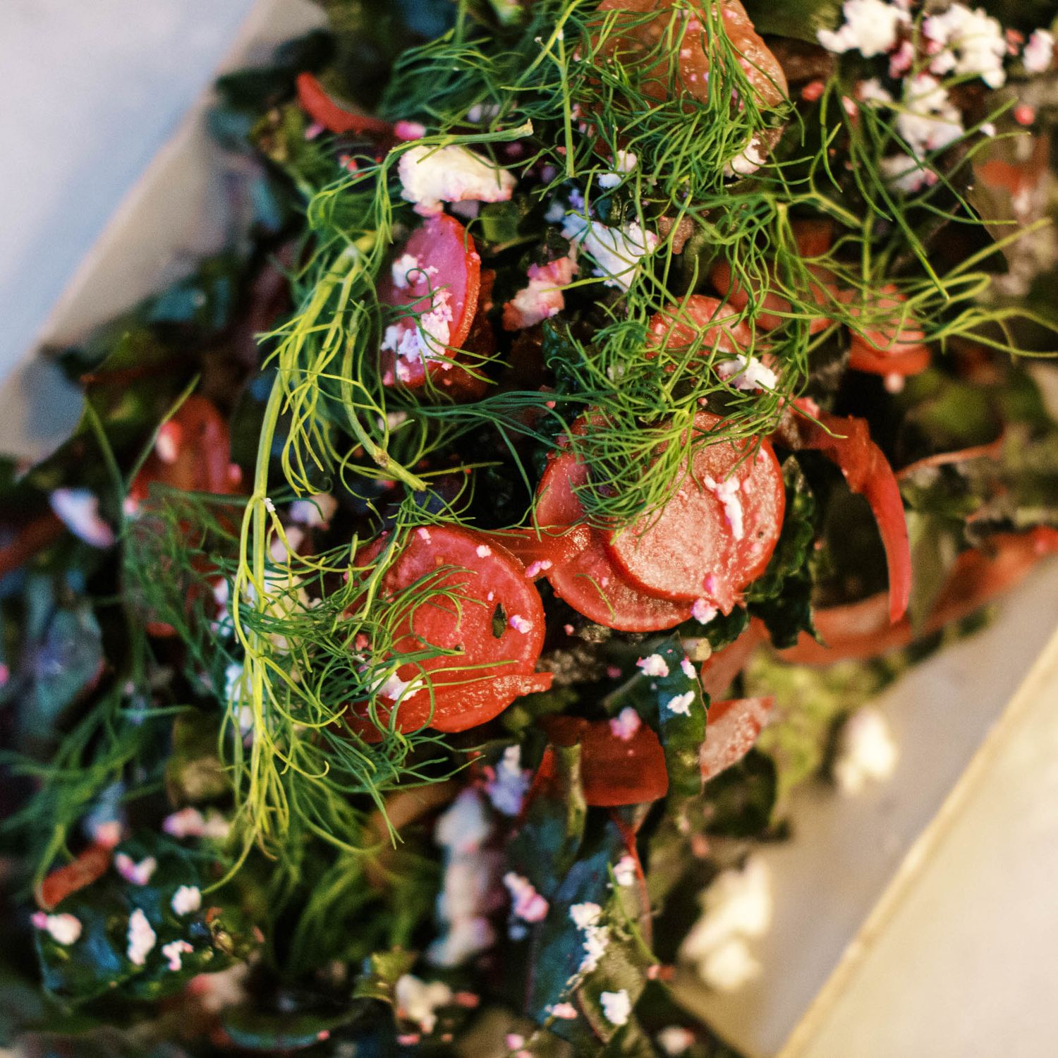 Fresh salad with sliced carrots, dark leafy greens, dill, red onion, and crumbled cheese on a white plate.