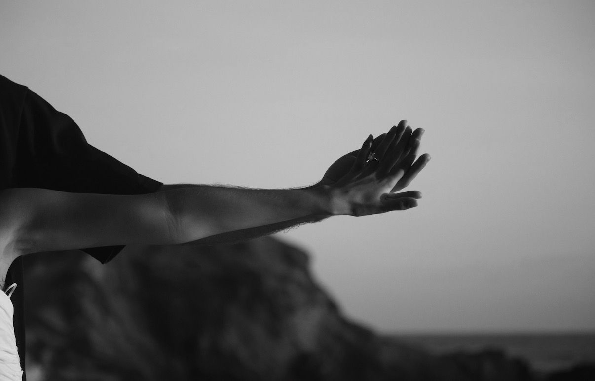 Black and white photo of a person extending their arm outward against a misty sky.
