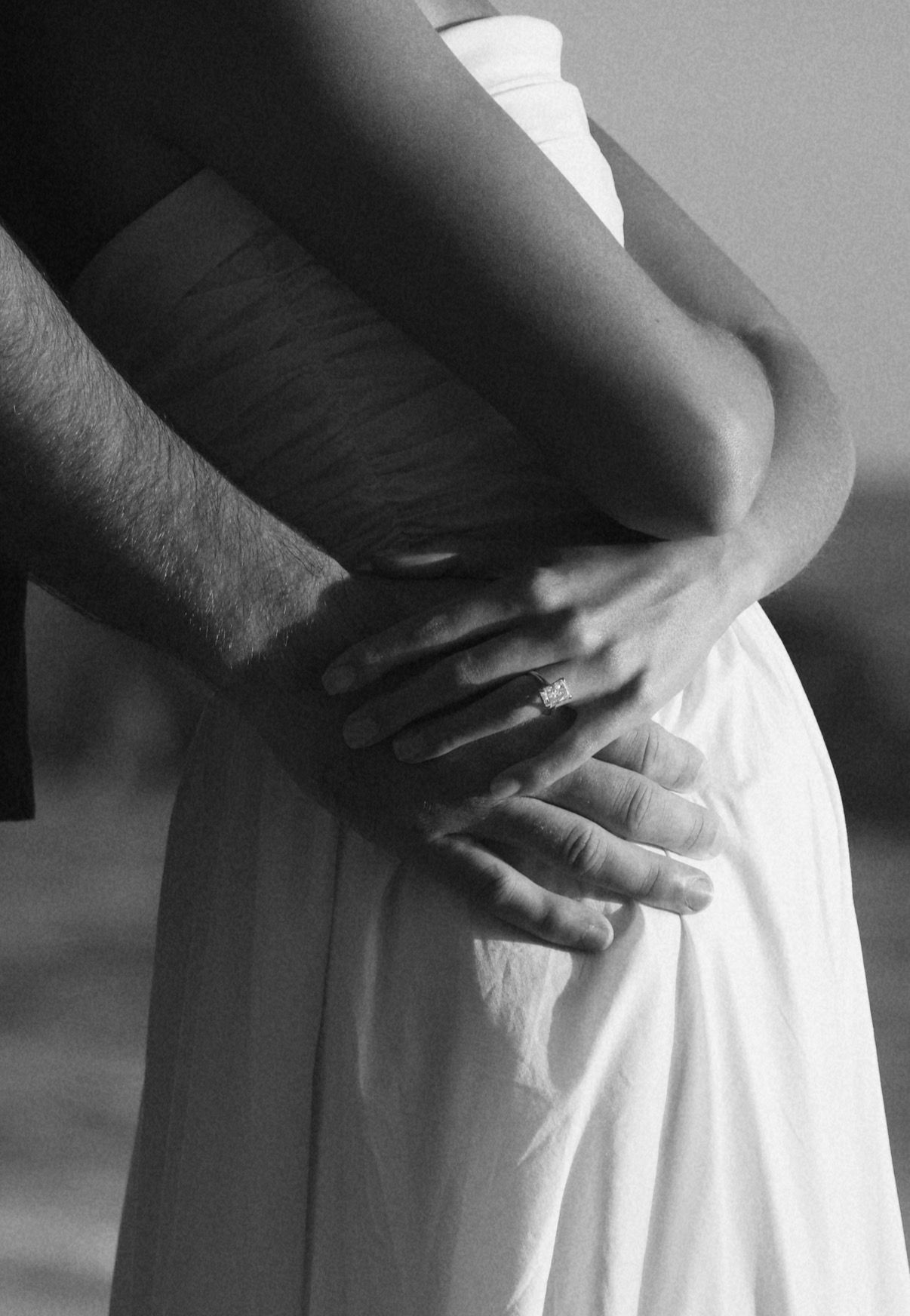 Black and white close-up of a couple embracing, woman wearing an engagement ring.