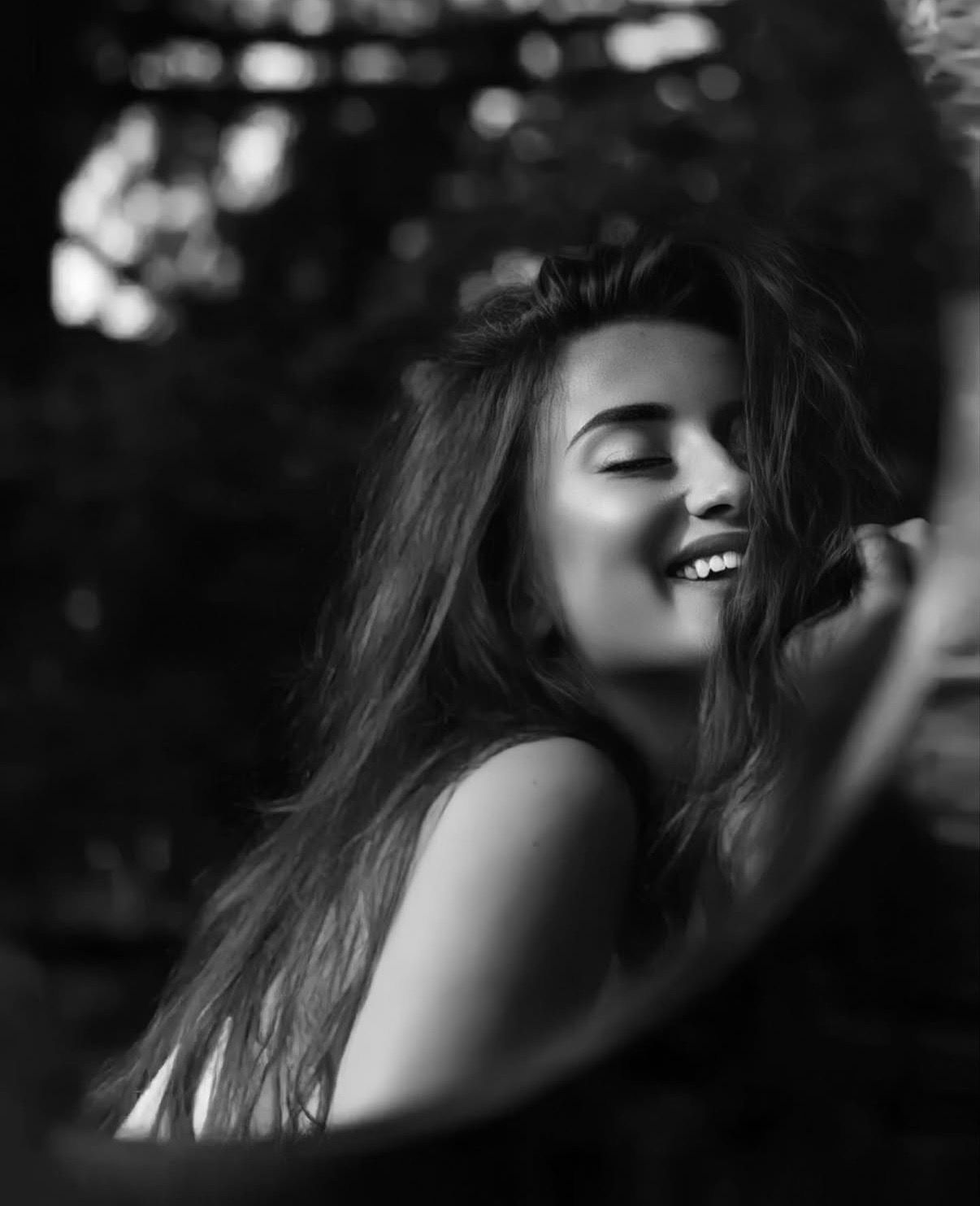 Black and white portrait of a smiling young woman with long hair enjoying a breezy outdoor moment.