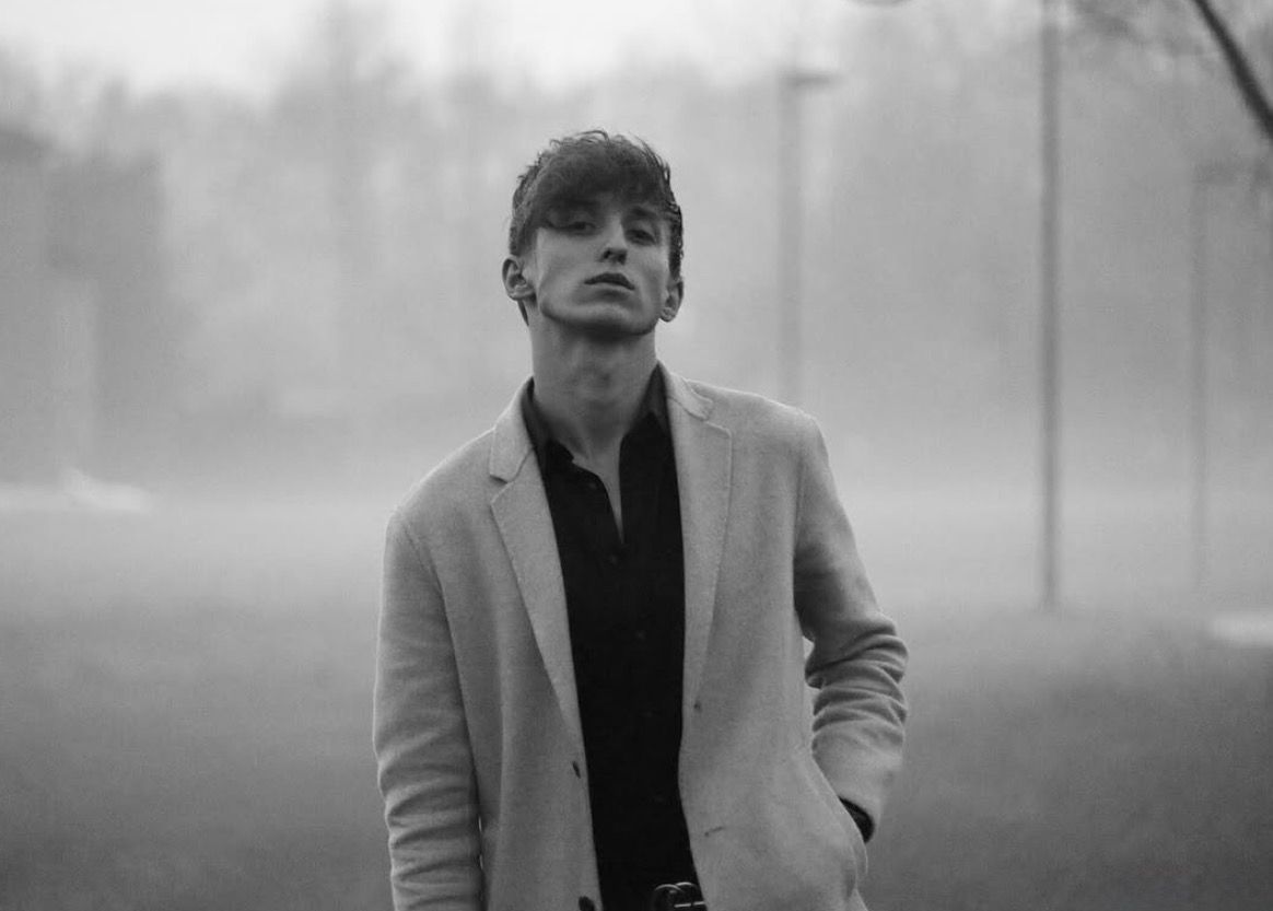 Young man in light blazer stands outdoors in foggy landscape, black and white portrait photography.