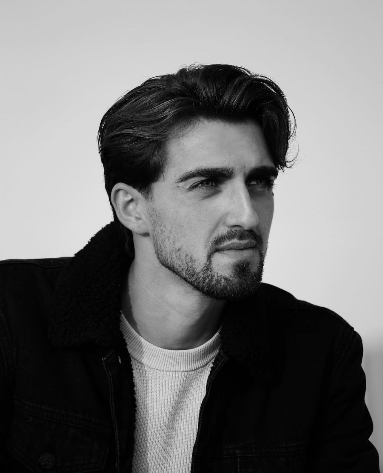 Black and white close-up portrait of a handsome bearded man with styled hair looking sideways.