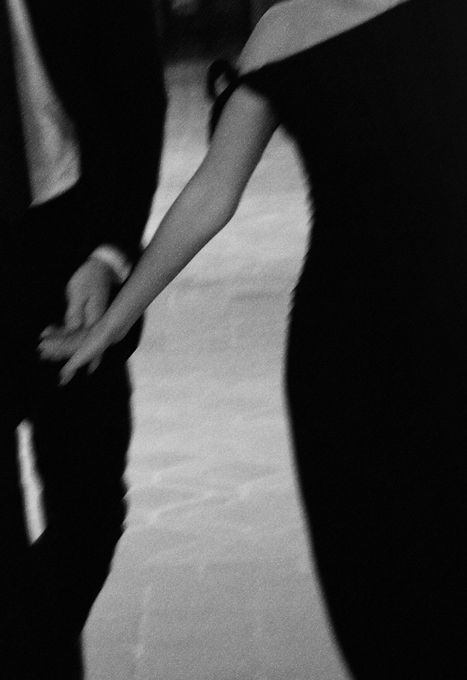 Black and white photo of two people holding hands, one in a white dress and one in a dark suit, captured in motion.