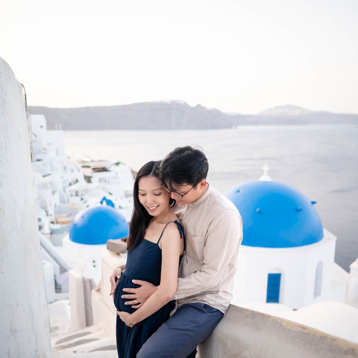 A couple posing for a maternity photo shoot in Oia village in Santorini next to the blue dome churches