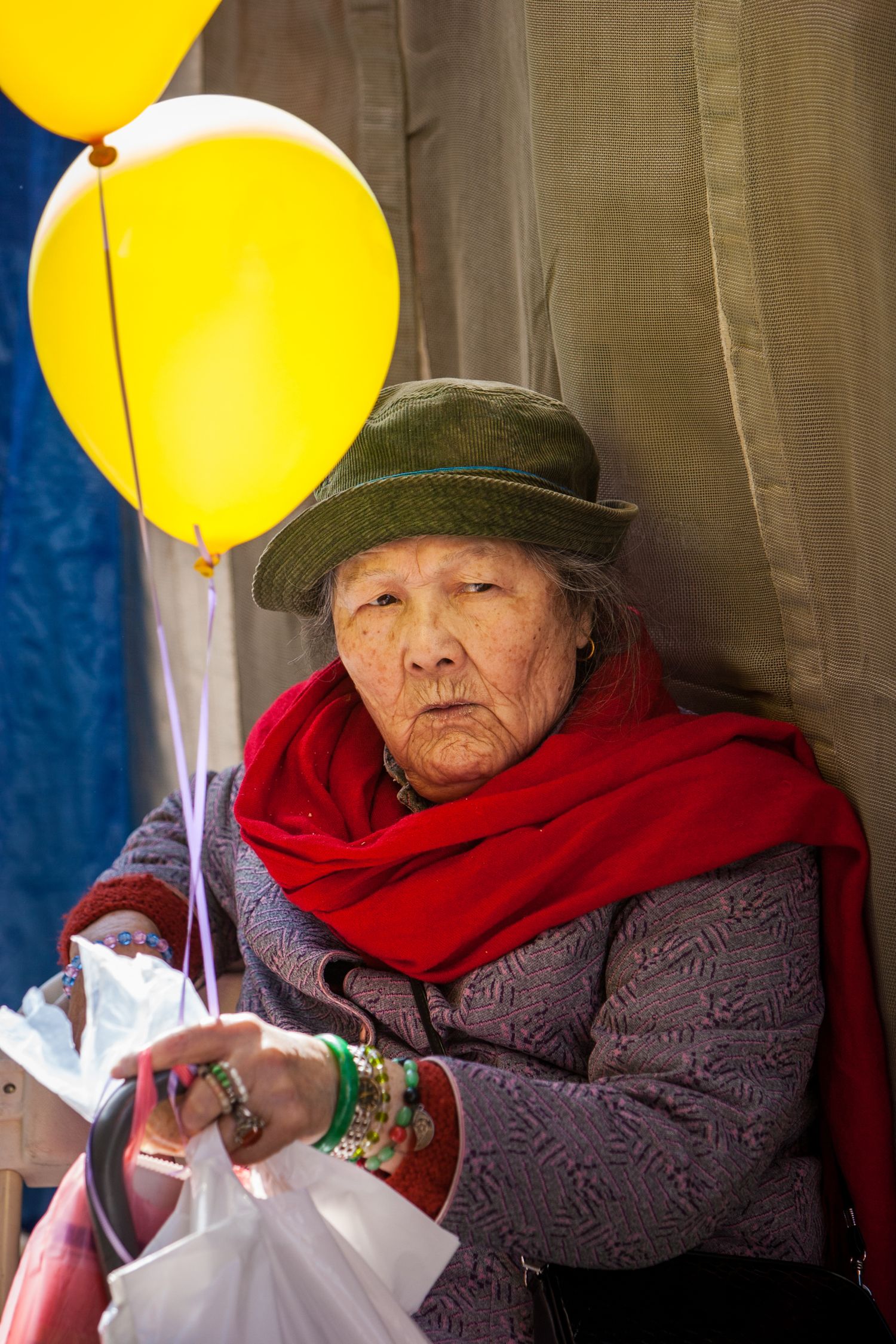 Elderly woman with yellow balloons and red scarf at a San Francisco Chinatown festival, captured in a candid street portrait.