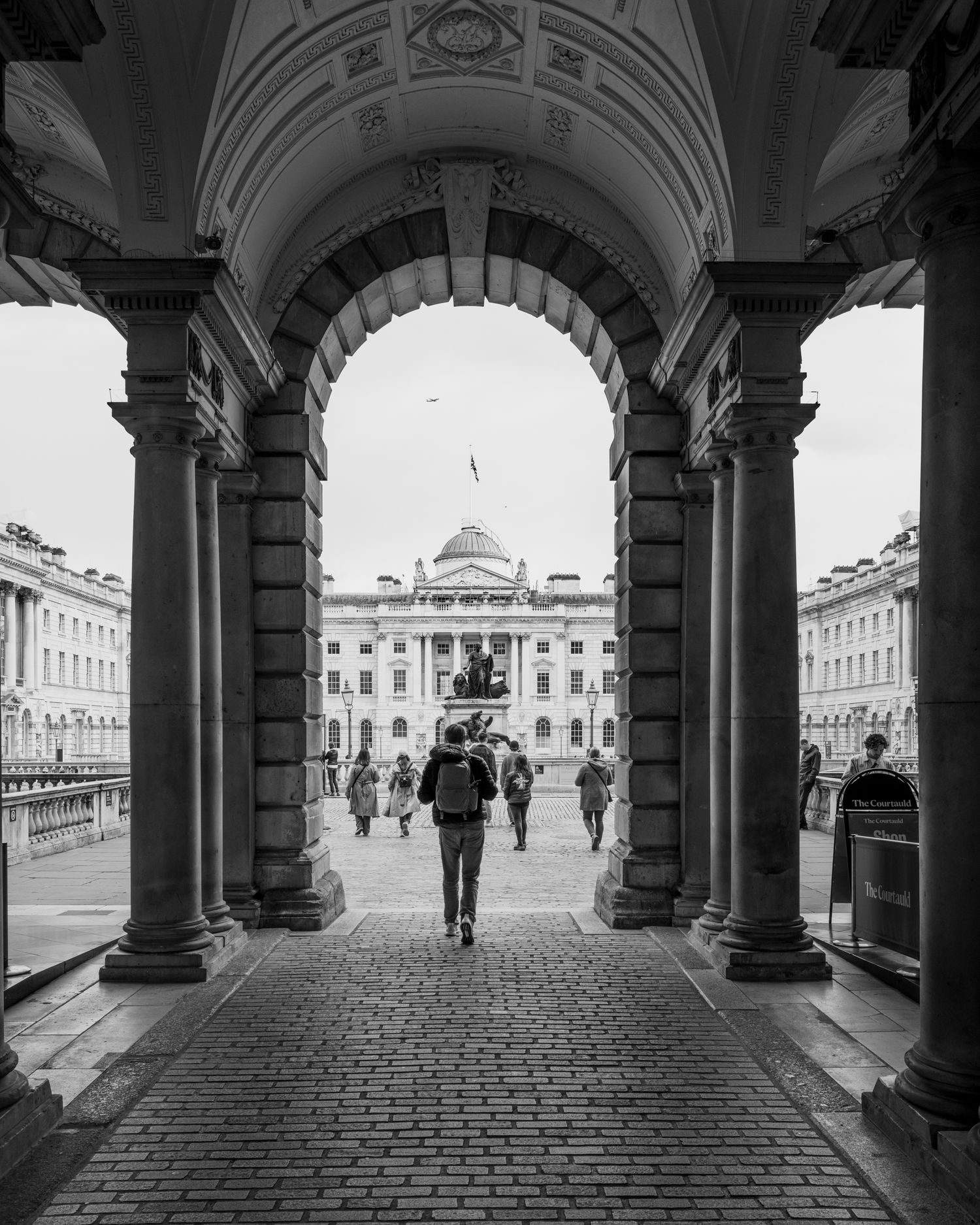 Pedestrian framed beneath Somerset House arches in London, highlighting symmetry, classical architecture, and street life.