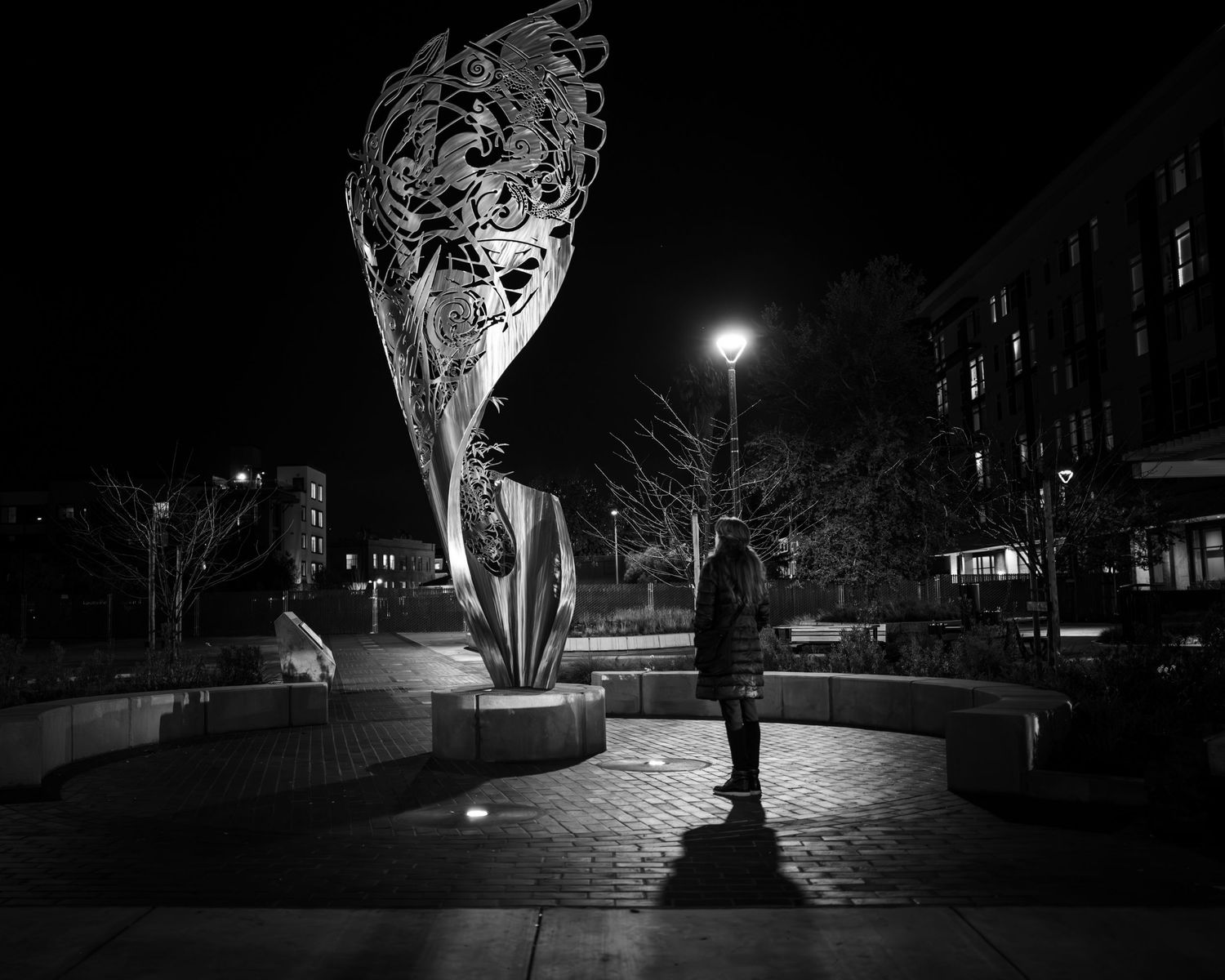 Solitary figure beneath illuminated sculpture in Japantown San Jose, captured in dramatic black and white night photography.