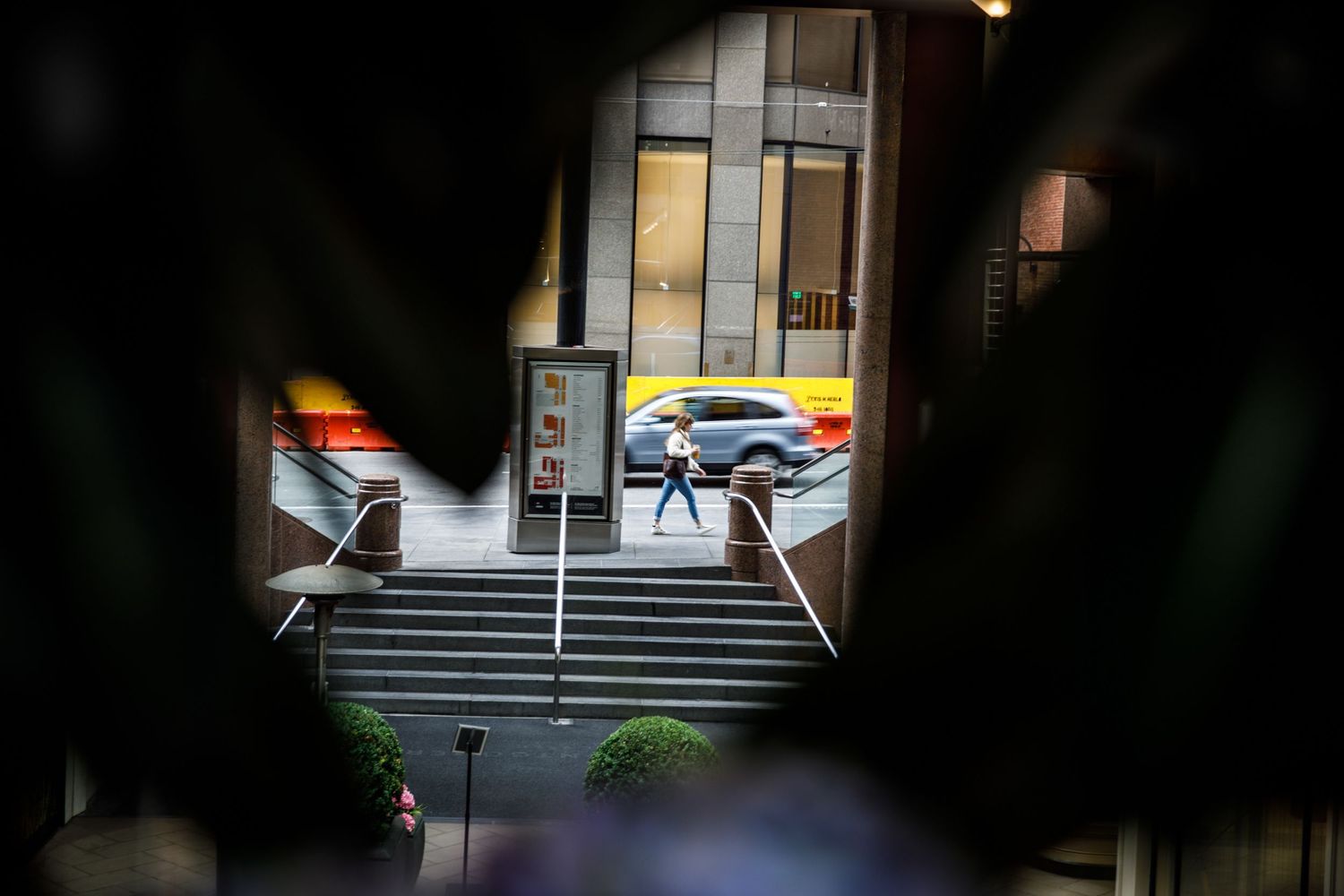 Pedestrian walks through downtown San Francisco, framed by dark foreground with passing traffic in a layered street scene.