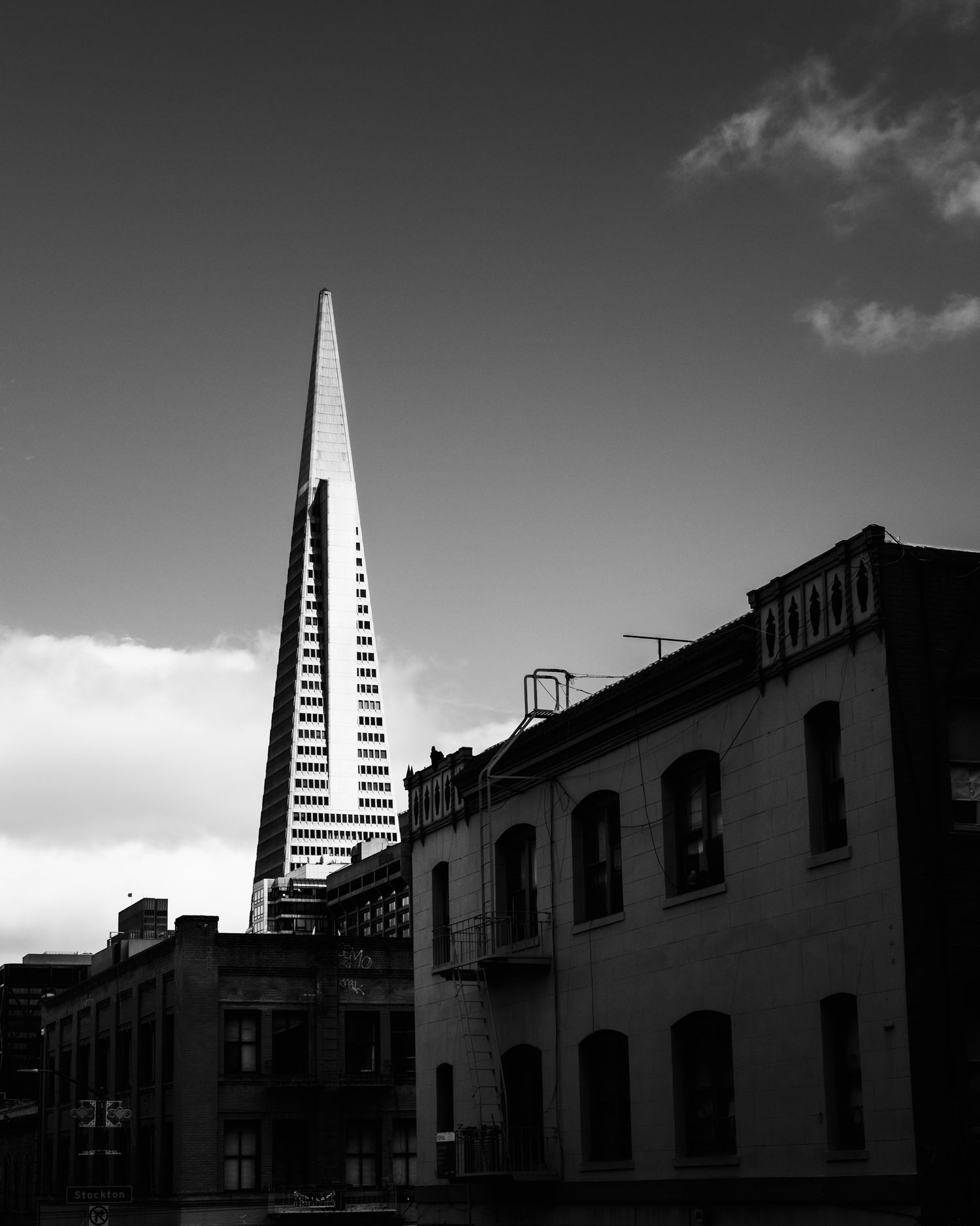 Black-and-white view of San Francisco's Transamerica Pyramid rising above historic buildings under a dramatic sky.