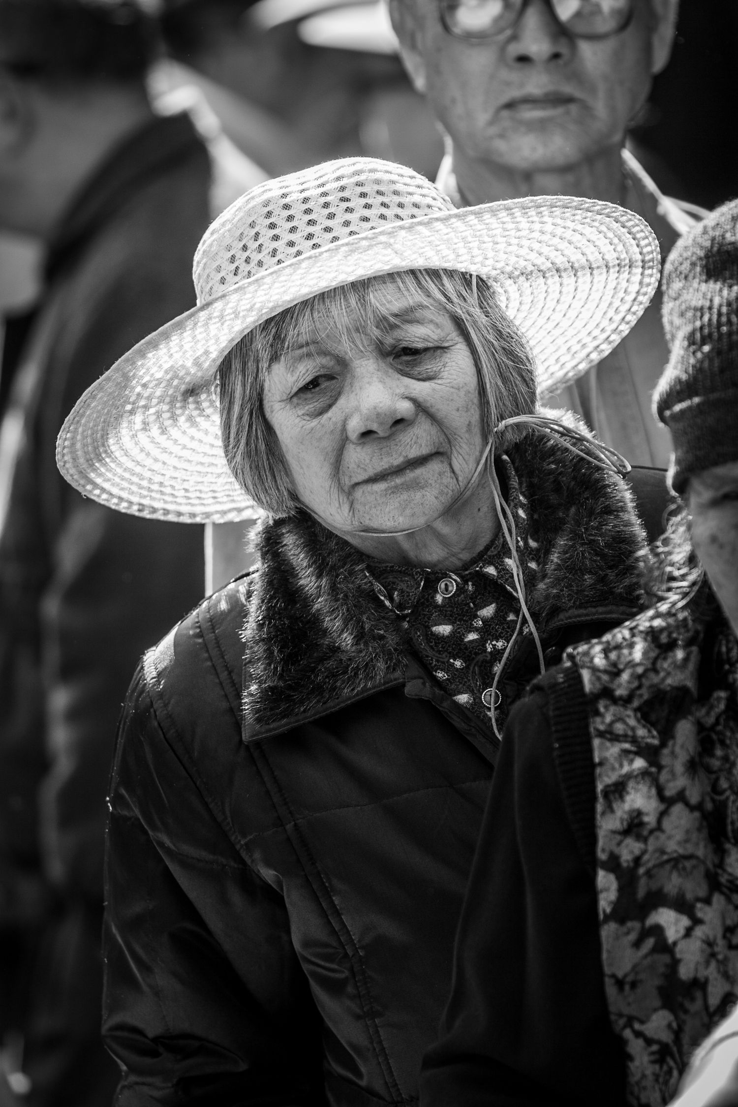 Thoughtful woman in a woven sun hat at a San Francisco Chinatown festival, captured in timeless black and white street photography.