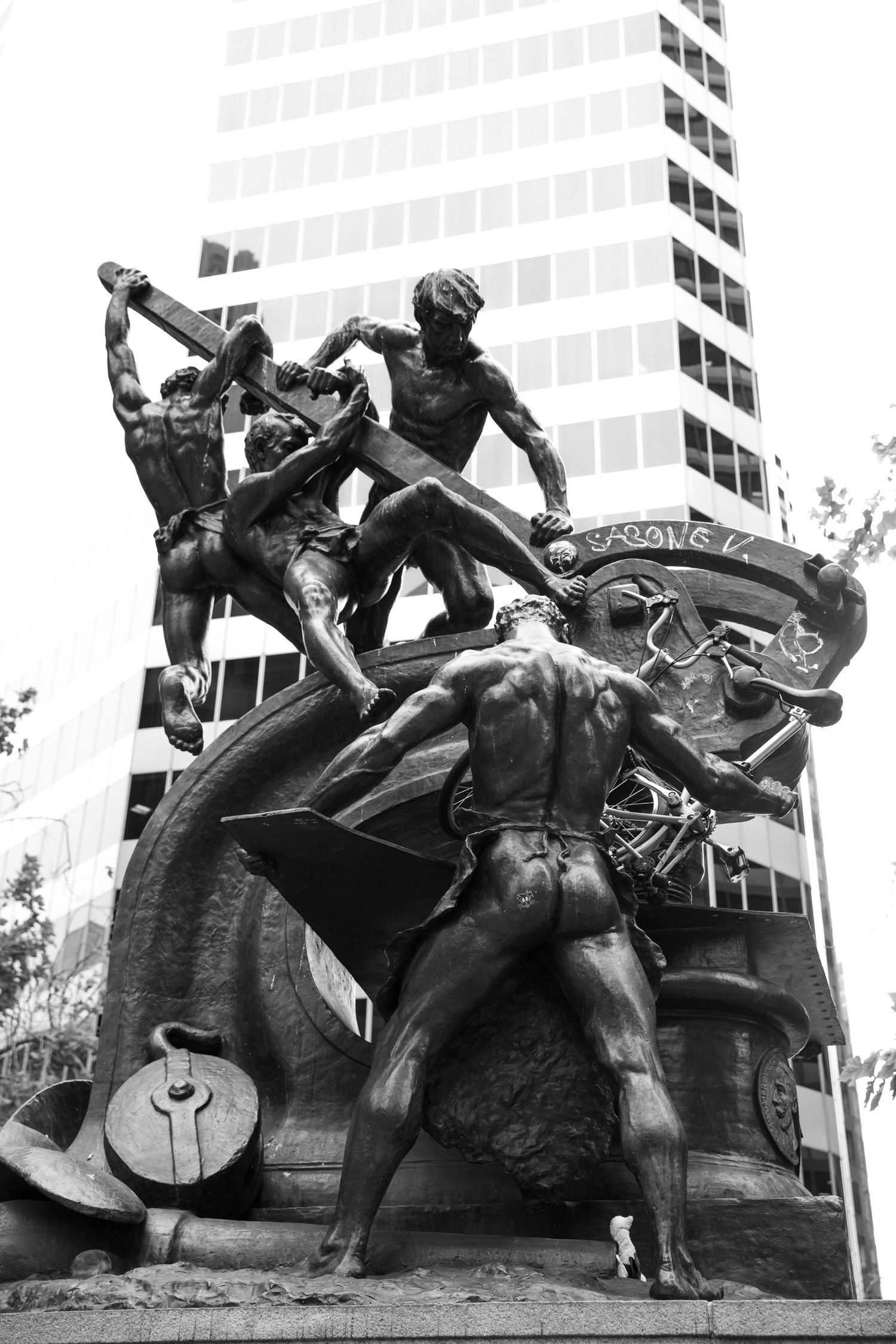 Black-and-white view of San Francisco's Mechanics Monument framed by a downtown skyscraper, blending history and urban design.