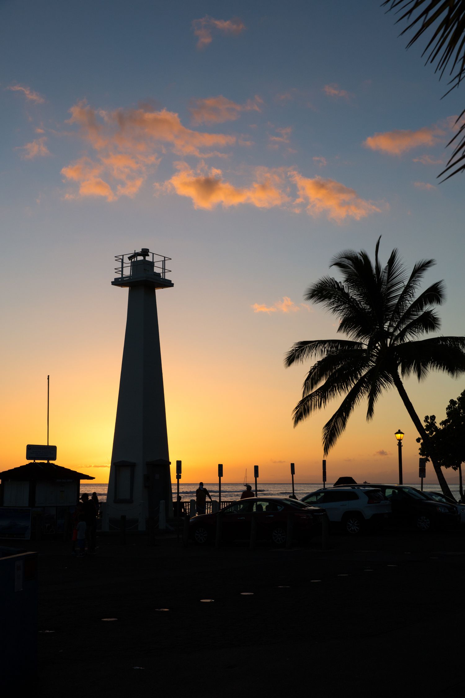 Silhouette of Lahaina Lighthouse and palm tree at sunset with glowing clouds over the Pacific Ocean in Lahaina, Maui, Hawaii.