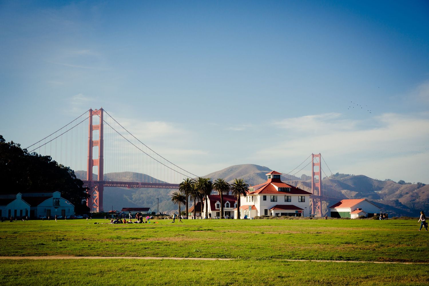 Golden Gate Bridge rising behind Crissy Field and its historic buildings, with palm trees and Marin Headlands in San Francisco.