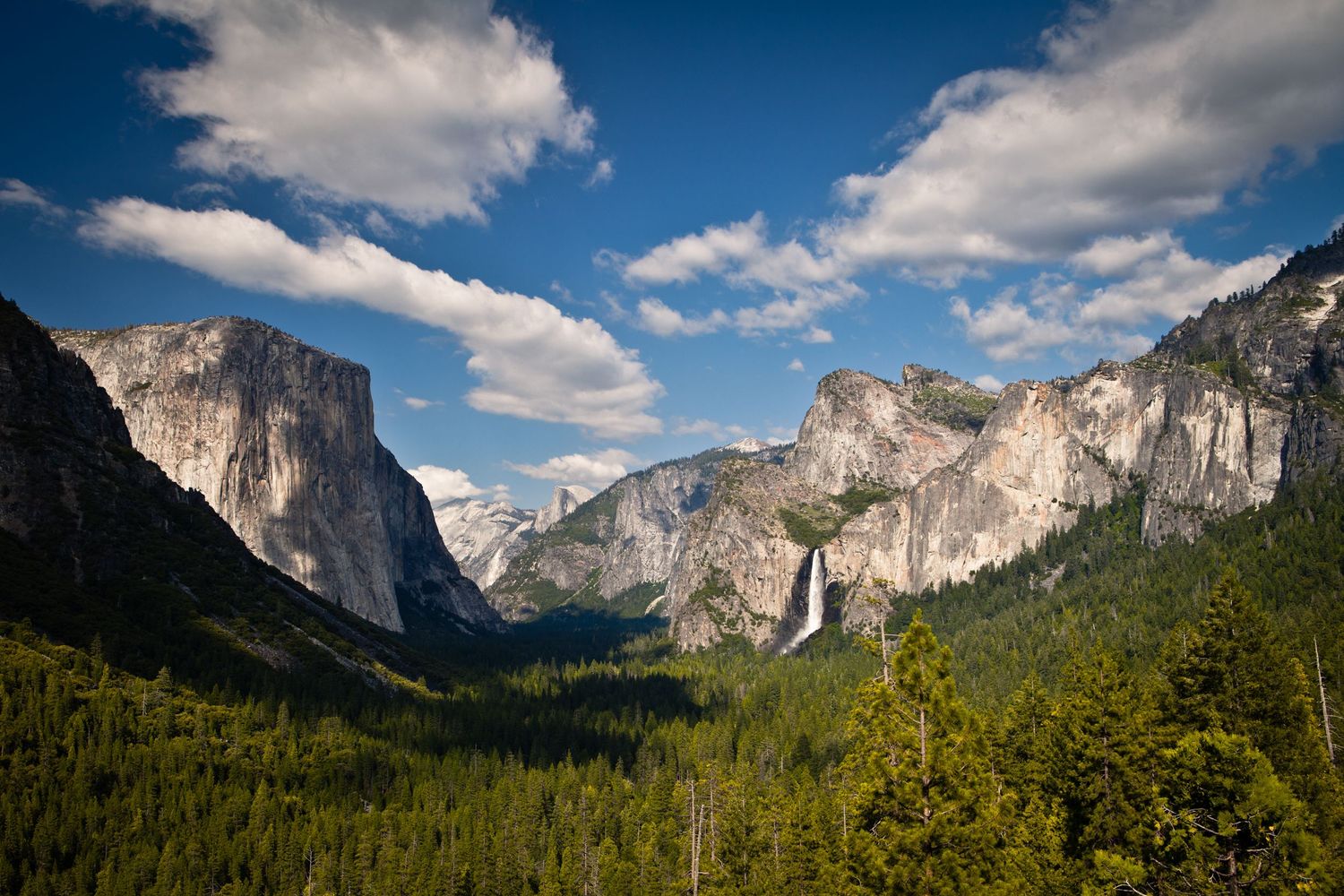 Panoramic view of Yosemite Valley from Tunnel View with El Capitan, Bridalveil Fall, Half Dome, and dramatic clouds overhead.