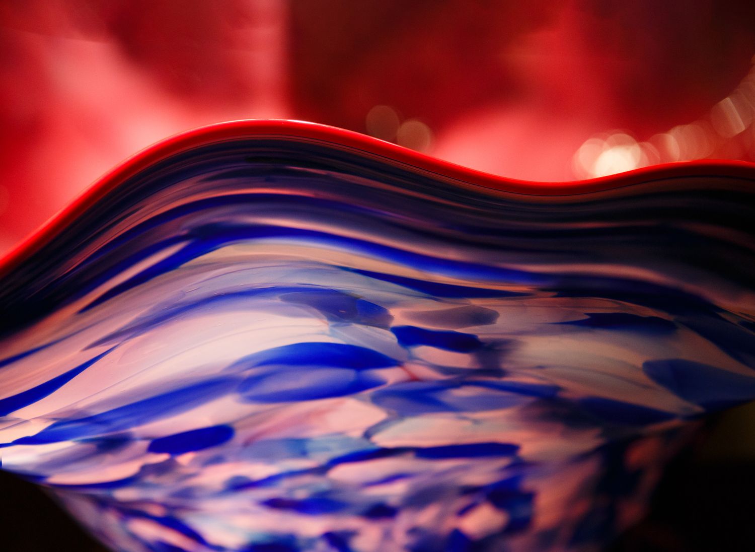Macro abstract of a Chihuly glass vase with flowing red and blue curves, luminous reflections, and vibrant fine art detail.