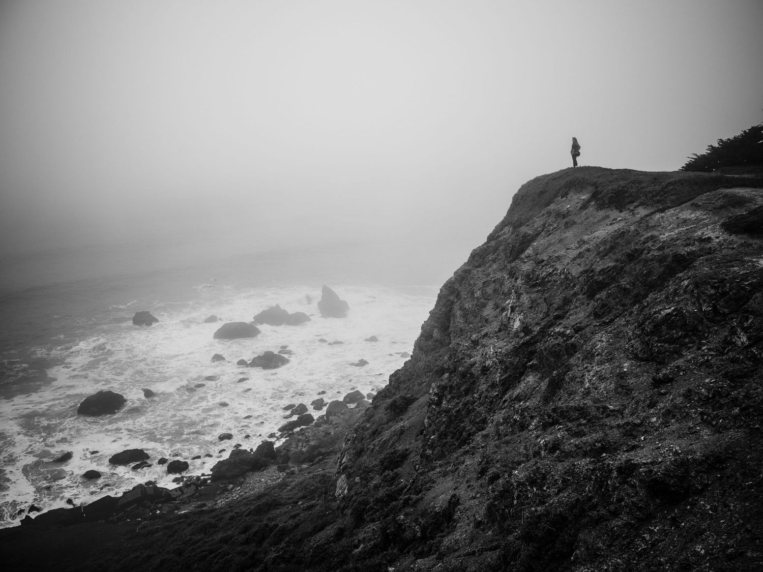 Lone figure overlooks the foggy cliffs and crashing Pacific Ocean at Linda Mar Rockaway Beach in Pacifica, California.
