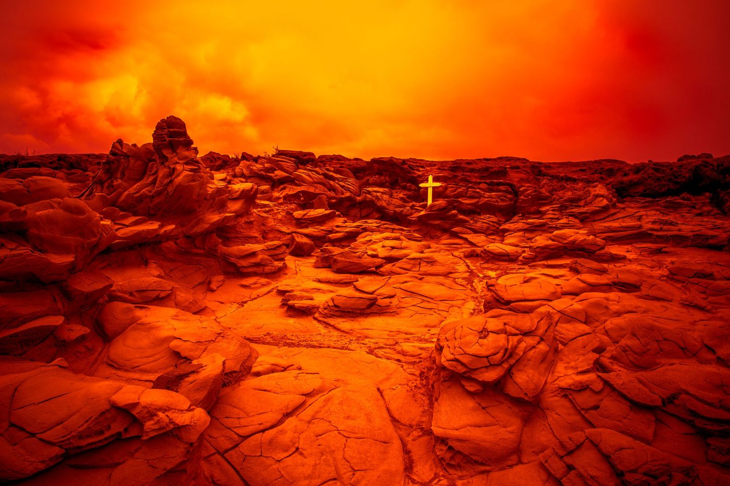 Fine art view of a white cross at Makaluapuna Point (Dragon's Teeth), Maui, glowing beneath a fiery orange sky.