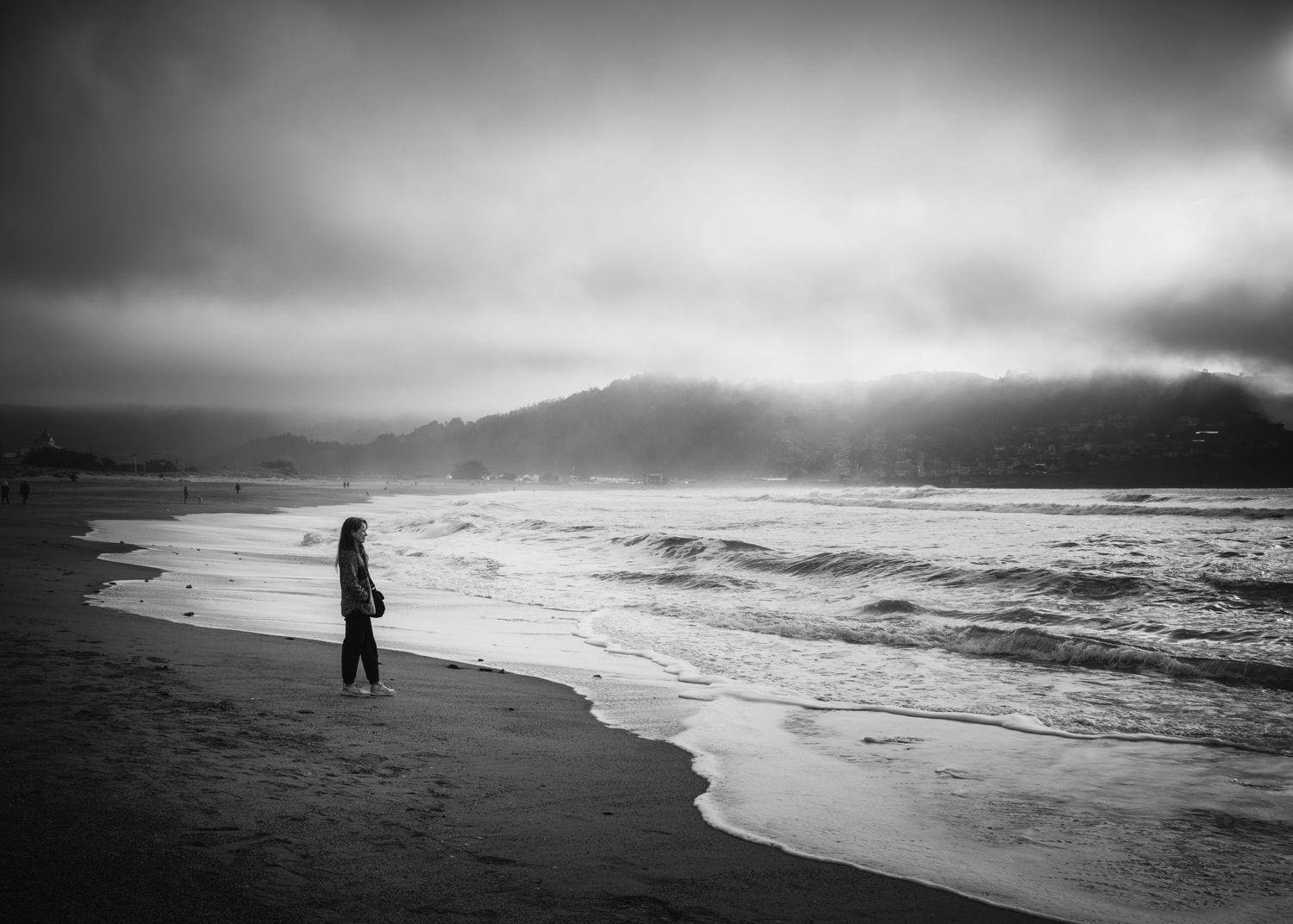 Solitary figure watching waves beneath dramatic storm clouds at Pacifica State Beach in Pacifica, California.