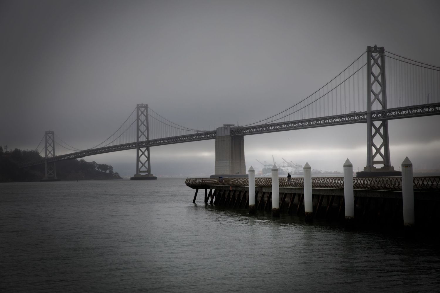 Fog-covered San Francisco Bay Bridge viewed from the waterfront on a moody morning, photographed by Bay Area photographer FotoMunki.