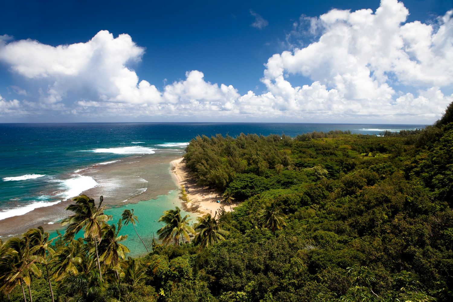 Panoramic view of Keʻe Beach on Kauaʻi, Hawaii, with turquoise water, lush tropical forest, coral reef, and dramatic clouds.