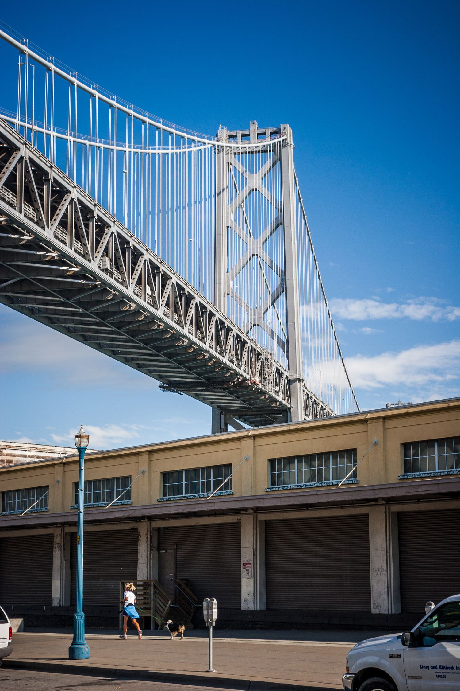 San Francisco Bay Bridge tower rising above waterfront warehouses under a clear blue California sky.
