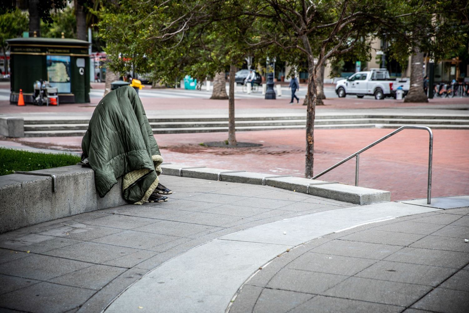 Blanket-covered figure resting in a San Francisco plaza, highlighting urban isolation through candid street photography.
