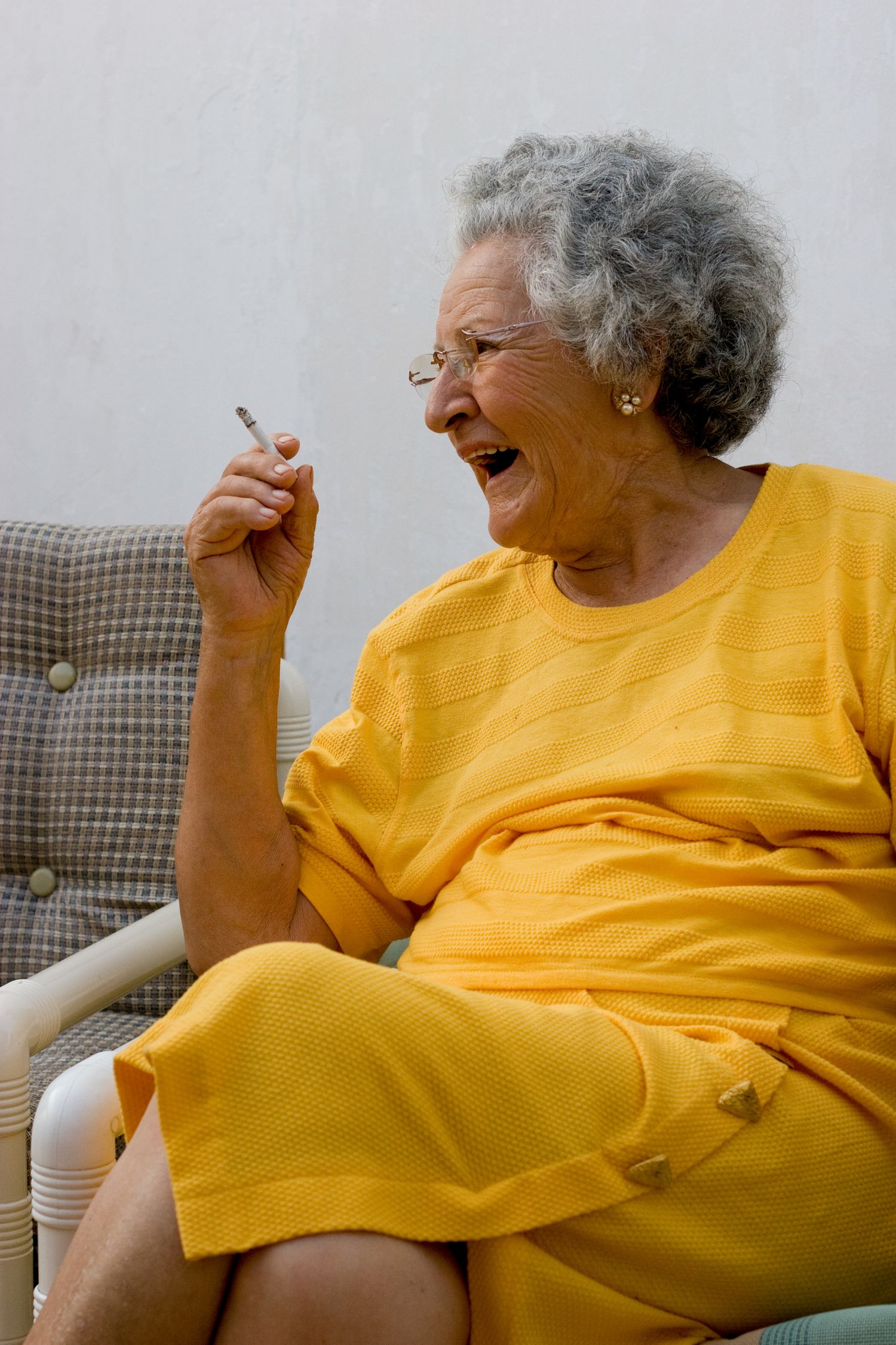 Laughing woman in a yellow dress holding a cigarette during a candid street portrait in Peru, celebrating everyday life.