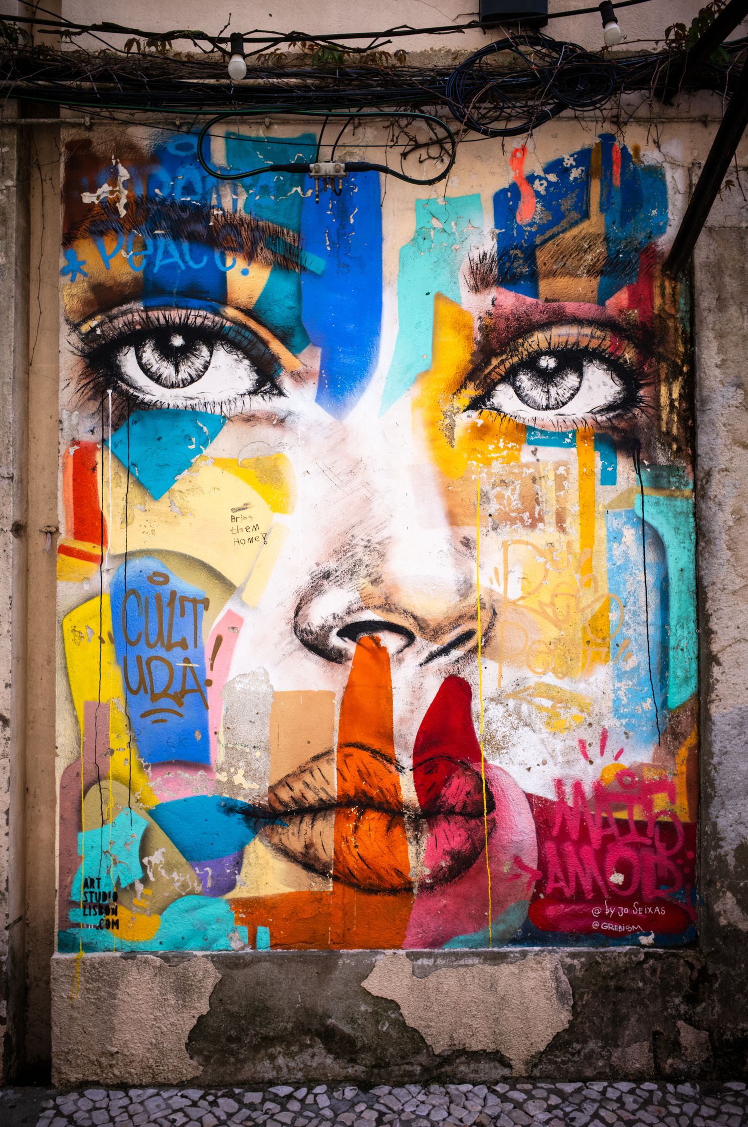 Colorful street art portrait with expressive eyes on a weathered wall at LX Factory in Lisbon, Portugal, captured as street photography.