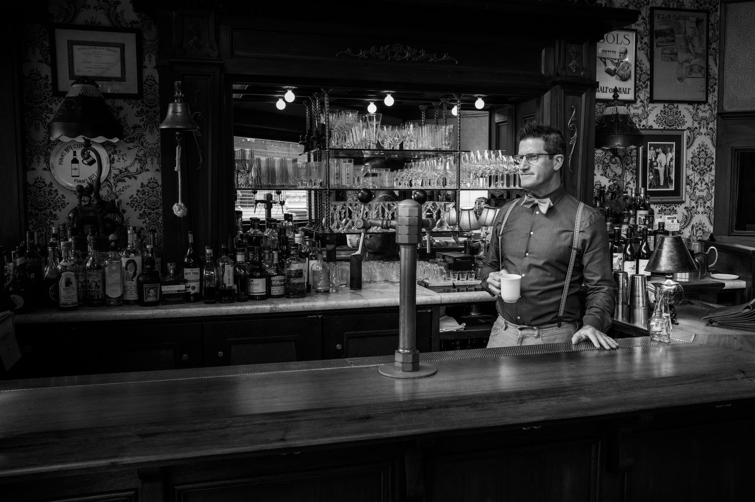 Bartender enjoying a quiet coffee behind the historic bar at Comstock Saloon in San Francisco, captured in black-and-white.