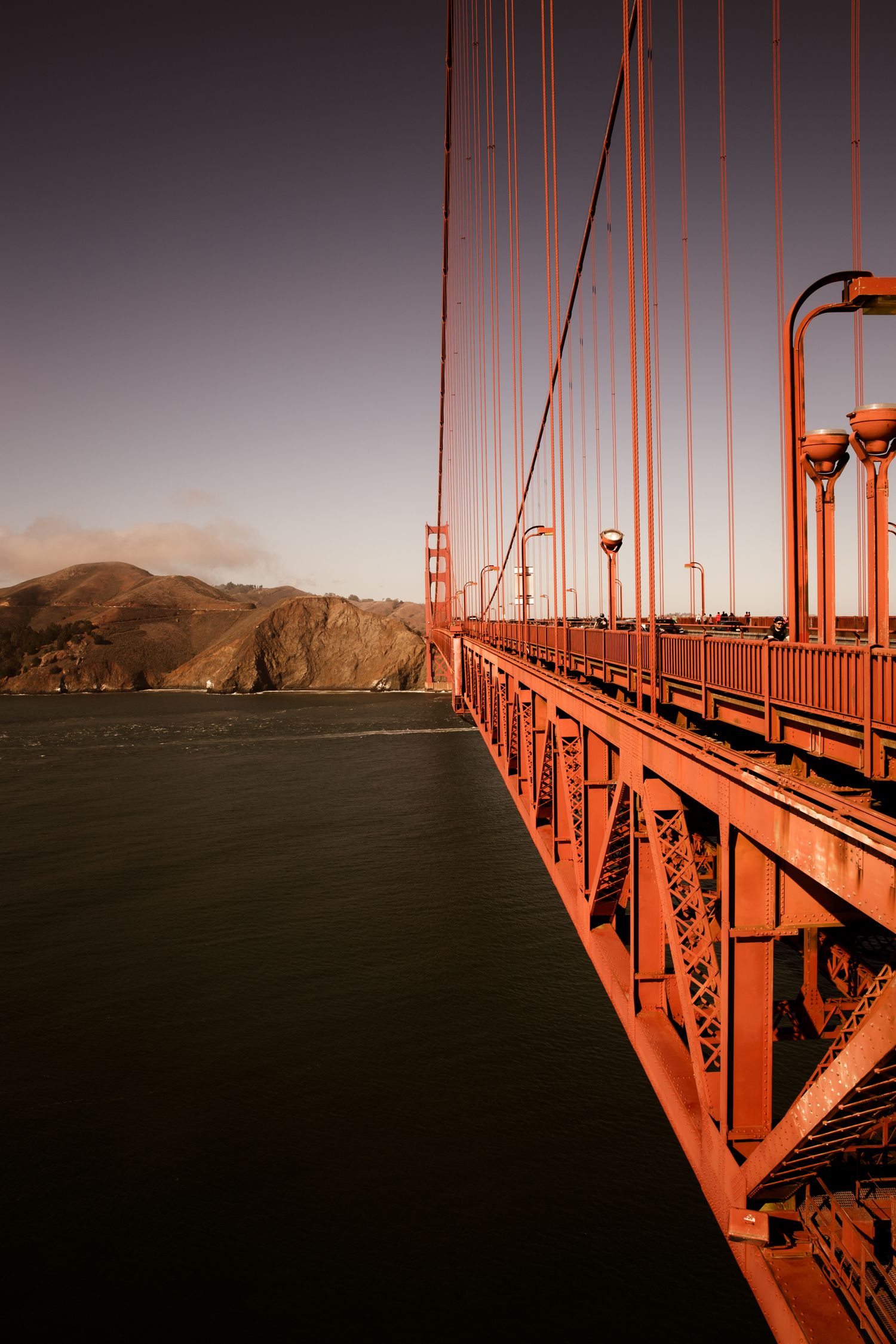 Golden Gate Bridge suspension cables and bridge deck leading toward Marin Headlands in warm afternoon light, San Francisco.