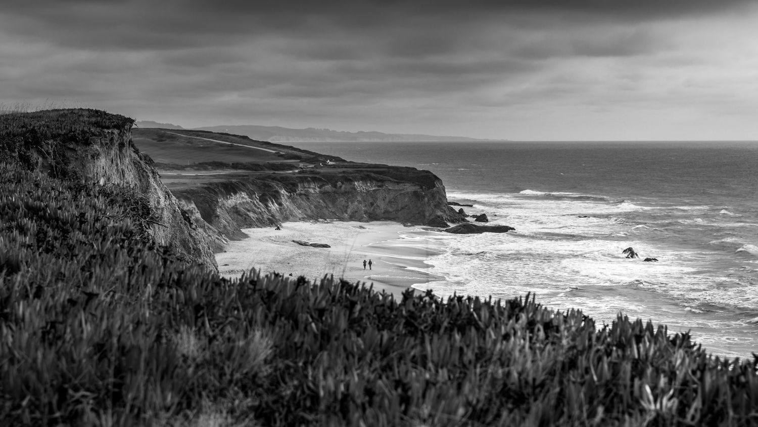 Black and white view of rugged coastal cliffs and stormy Pacific shoreline near Half Moon Bay, California.