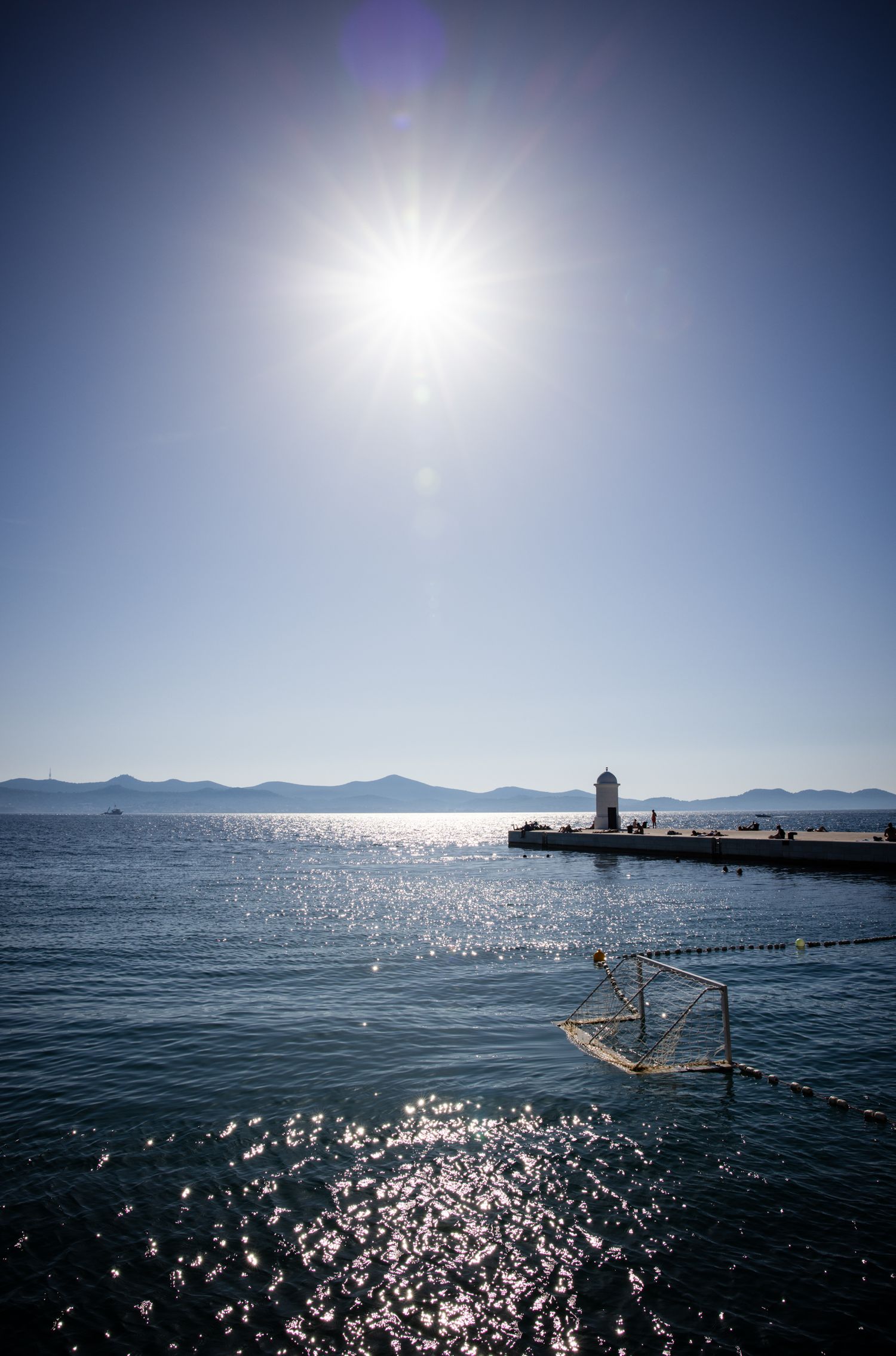 Sunburst over the Adriatic Sea in Zadar, Croatia, with sparkling water, a waterfront pier, and distant Dalmatian islands.