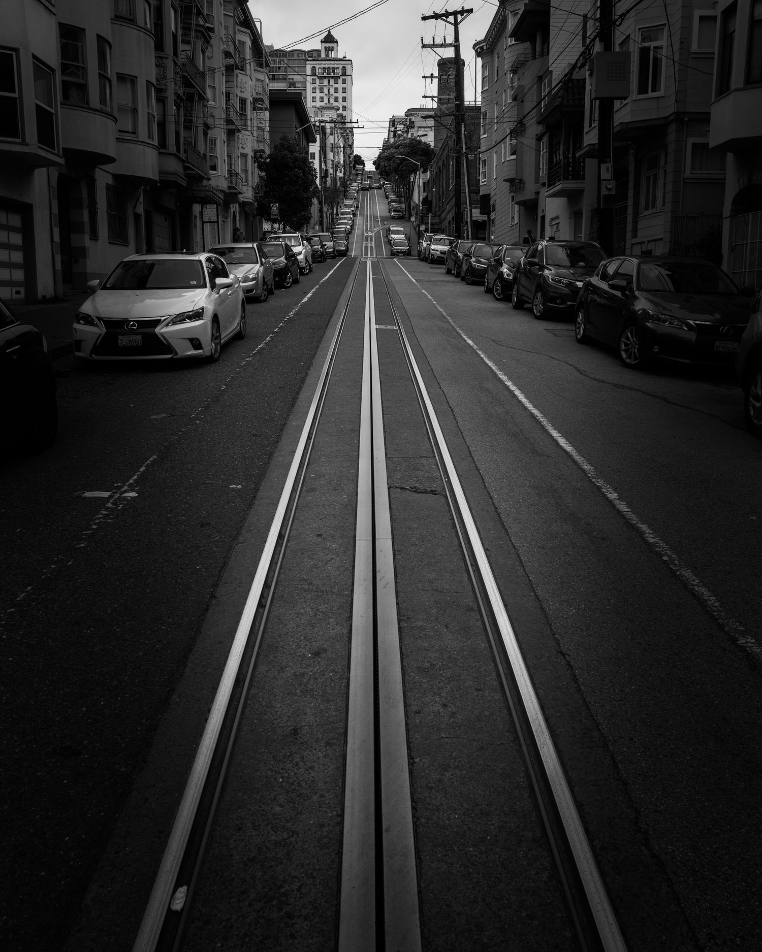 Black-and-white view of San Francisco cable car rails climbing a steep city street with striking leading lines and urban symmetry.