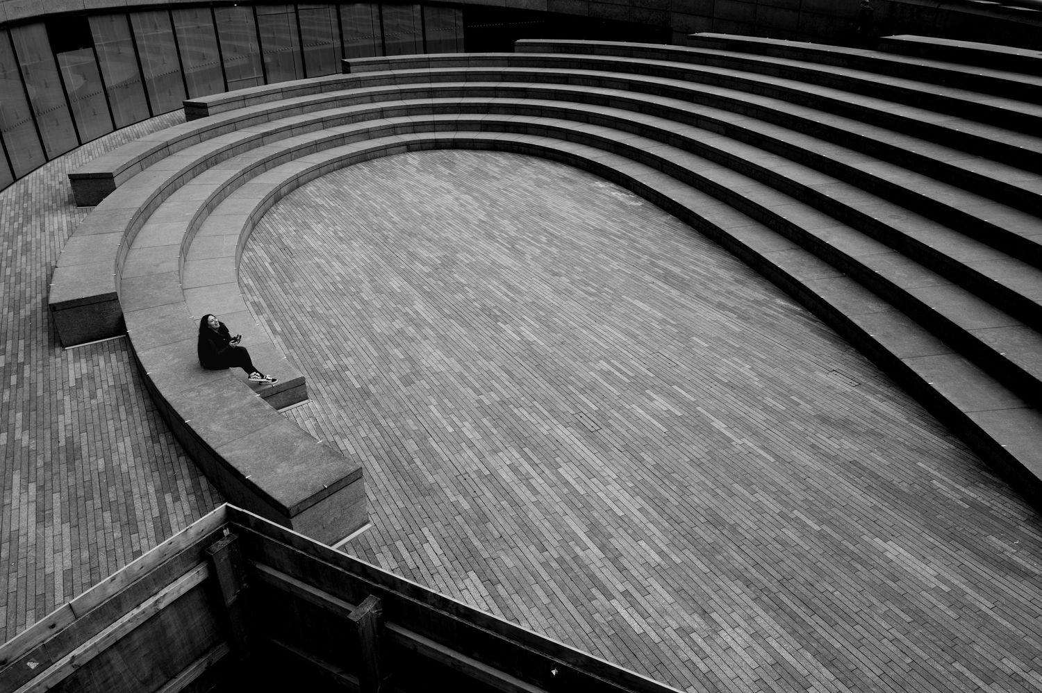 Lone person seated beside curved amphitheater steps along the Thames in London laughing, captured in minimalist black and white.