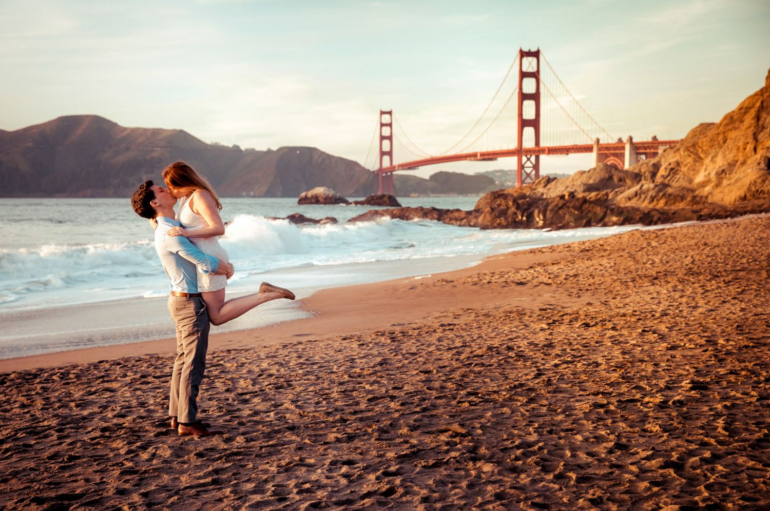Couple embracing at Baker Beach with the Golden Gate Bridge at sunset during a romantic San Francisco engagement session.