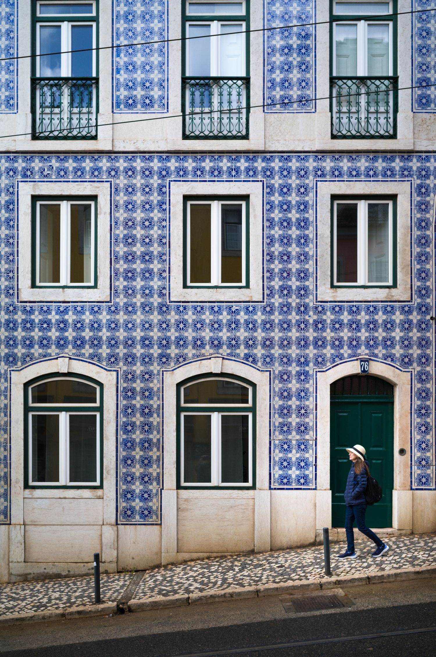 Woman in a white hat walks past a blue azulejo tiled building in Lisbon, Portugal, blending street photography with travel storytelling.