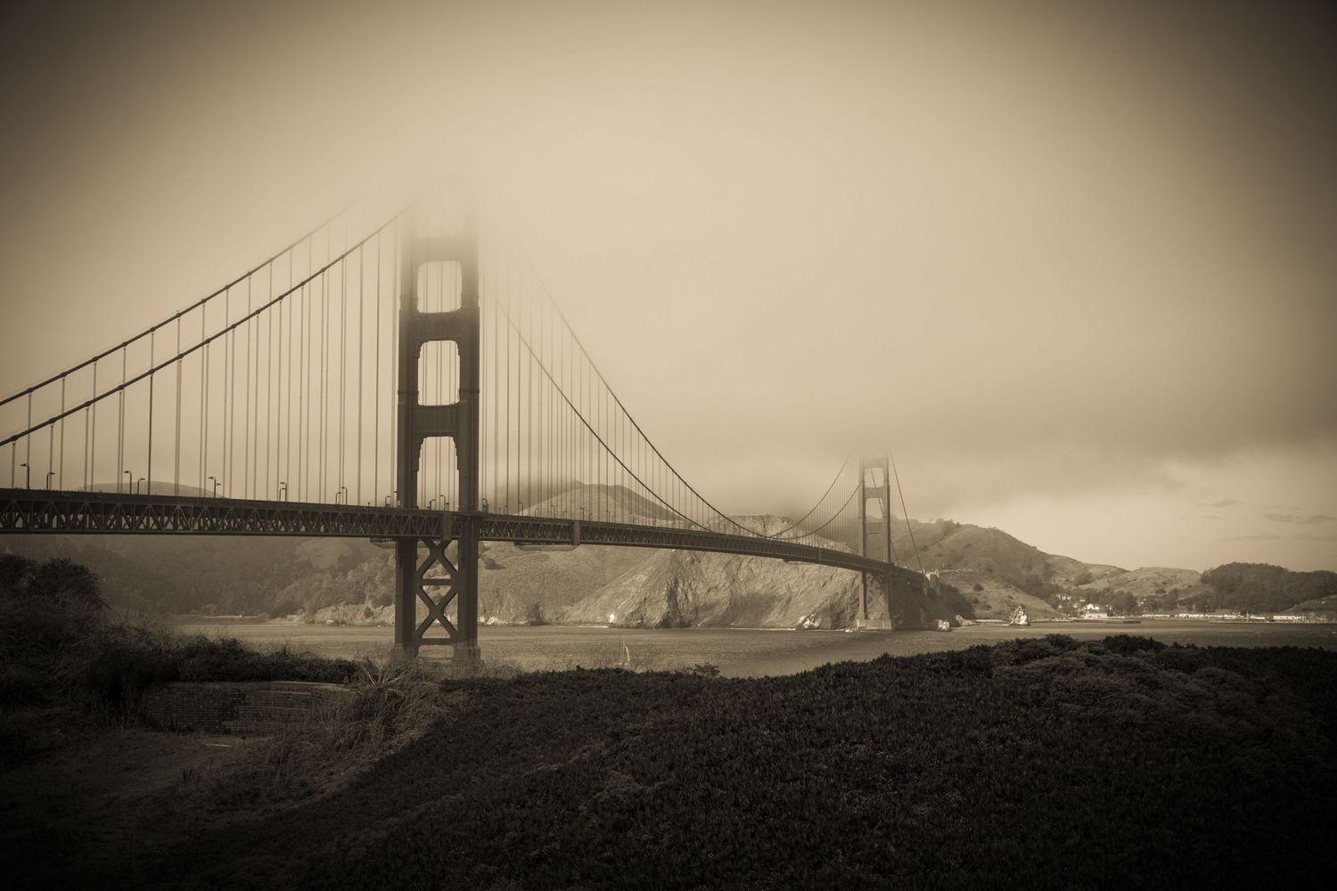 Sepia fine art view of the Golden Gate Bridge disappearing into dense fog with the Marin Headlands in the background.