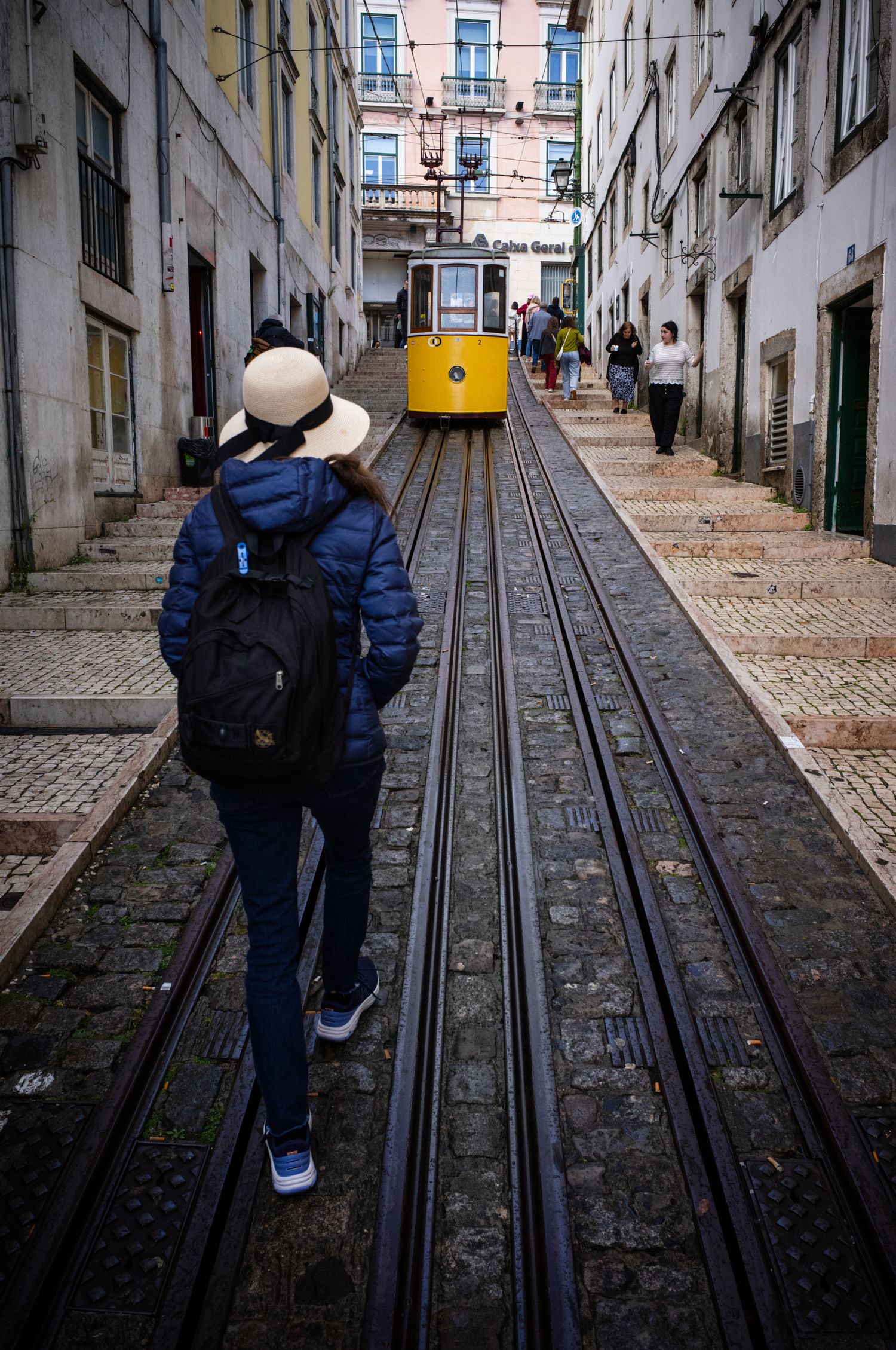 Woman in a sun hat walking toward Lisbon's Elevador da Glória funicular, capturing the spirit of travel in Portugal's historic streets.