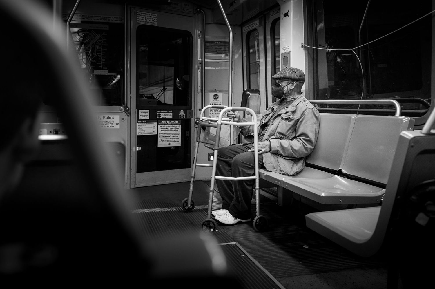 Solitary passenger with a walker rides a San Francisco BART train in a quiet black-and-white street photography moment.