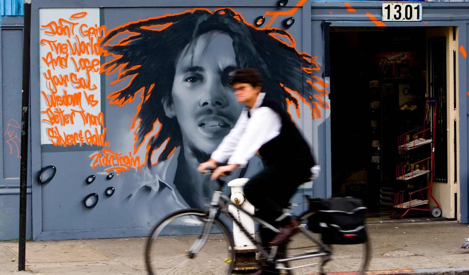 Cyclist speeds past a Bob Marley mural in San Francisco, blending street art, motion, and urban culture in a candid city scene.