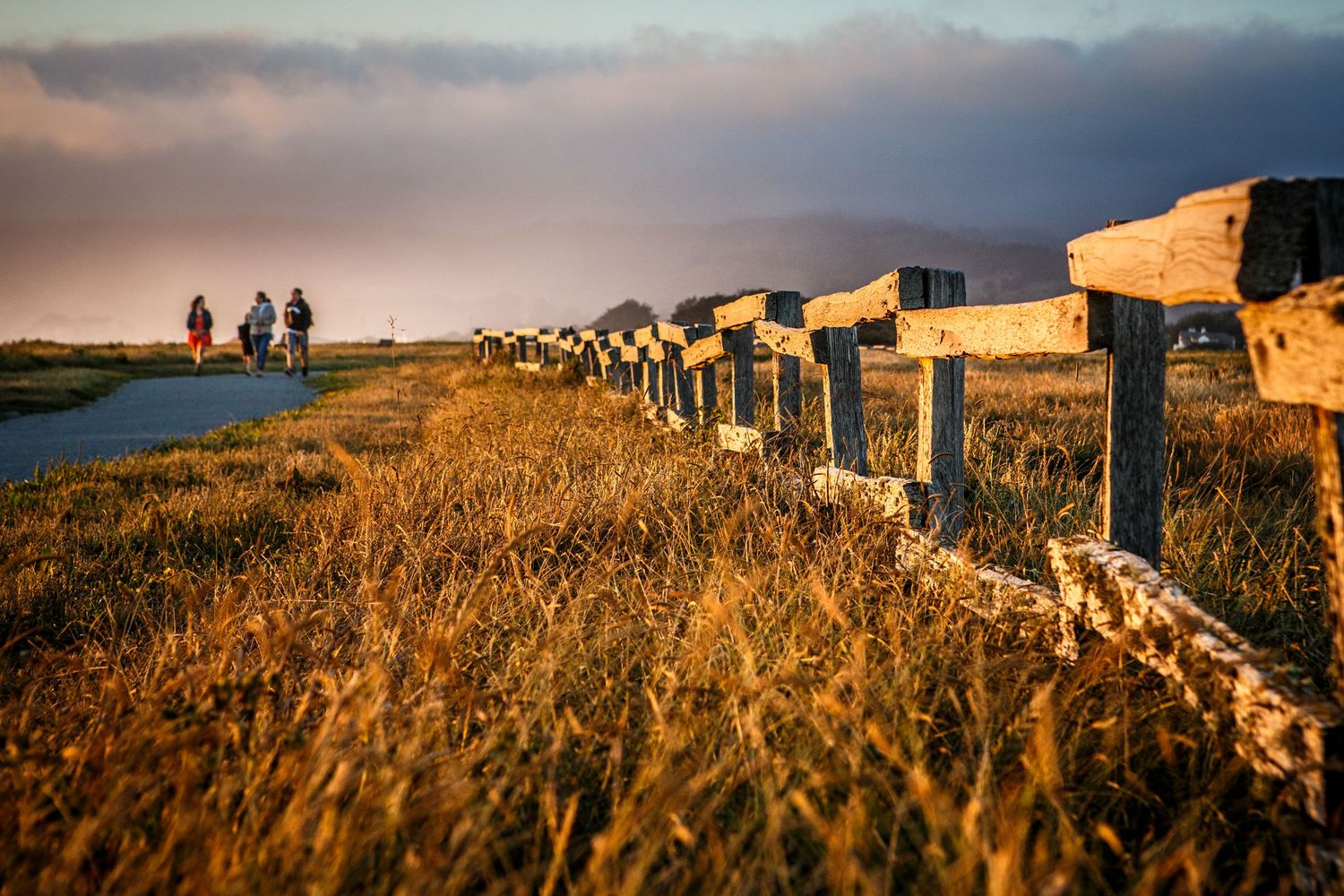Weathered fence glowing at golden hour along the coastal trail in Half Moon Bay, California, with walkers beneath rolling Pacific fog.