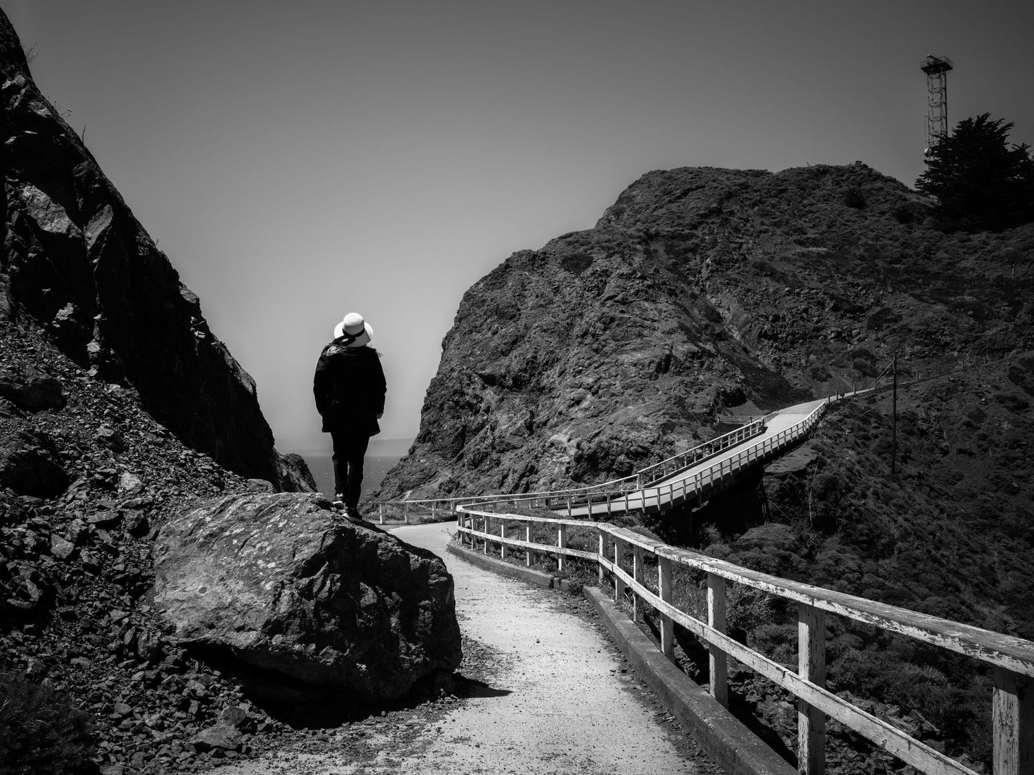 Woman in a white hat overlooks the trail to Point Bonita Lighthouse in the Marin Headlands near San Francisco, black and white.