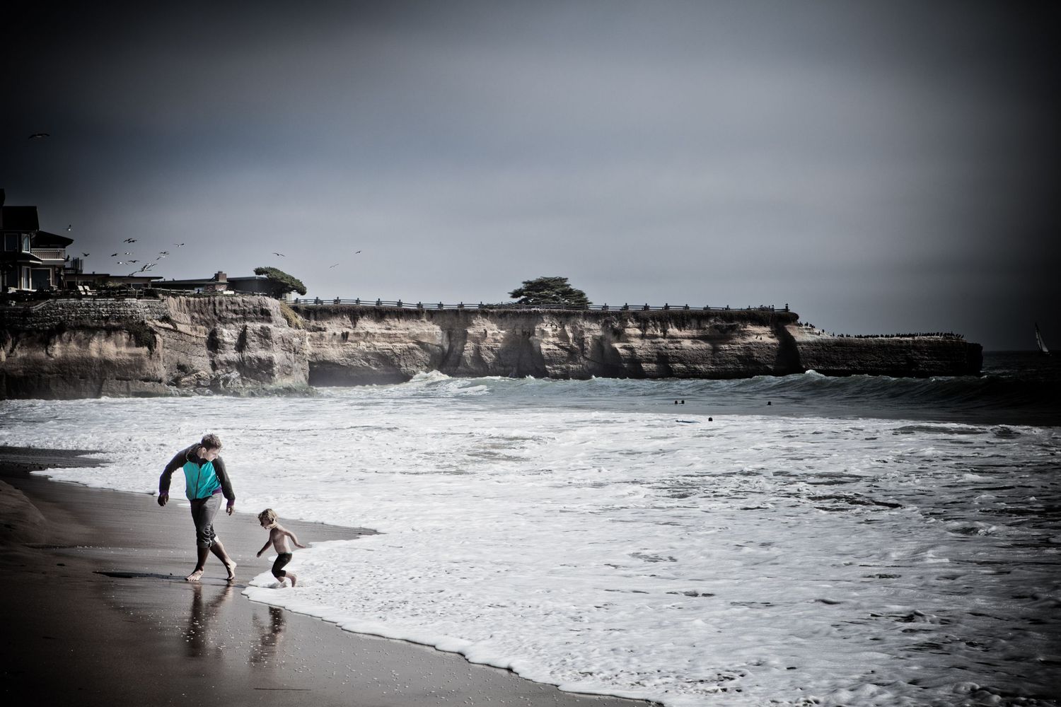 Father and daughter playing in the Pacific surf beneath the cliffs at Santa Cruz, California on a moody coastal afternoon.