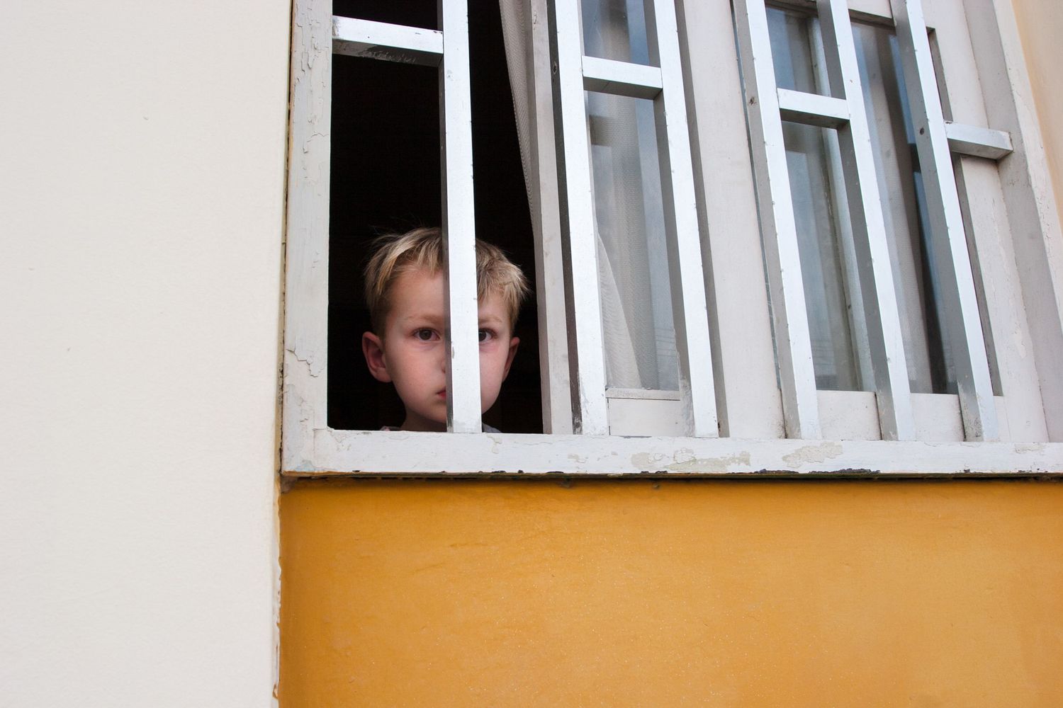 Child peers through a barred window in Peru, capturing a quiet moment of curiosity and everyday life in a candid street photograph.